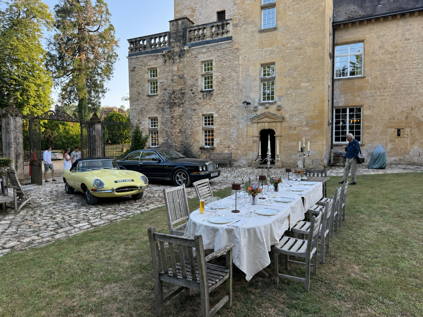 An outdoor dining table prepared beside classic cars at Château de Sermet